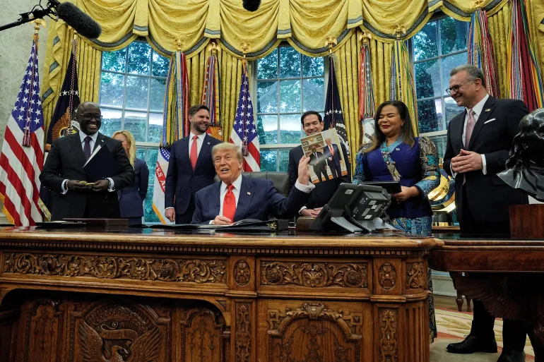 Donald Trump holds up a picture of himself with Rwanda's Foreign Minister Olivier Nduhungirehe on June 27, as leaders from Rwanda and the Democratic Republic of the Congo meet at the White House [Ken Cedeno/Reuters]