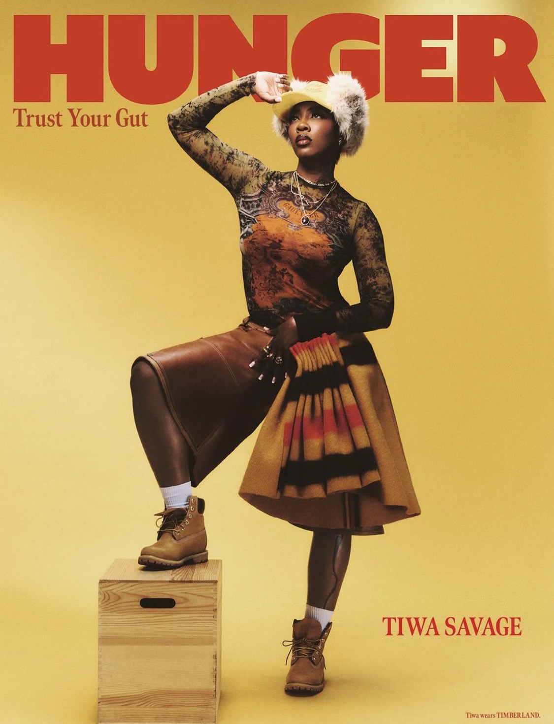 Tiwa Savage wears top by JEAN PAUL GAULTIER, hat by PARALLEL X STUDIO, earrings by ACCESSORIZE, rings by NEXT and shorter necklaces by H&M