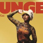 Tiwa Savage wears top by JEAN PAUL GAULTIER, hat by PARALLEL X STUDIO, earrings by ACCESSORIZE, rings by NEXT and shorter necklaces by H&M