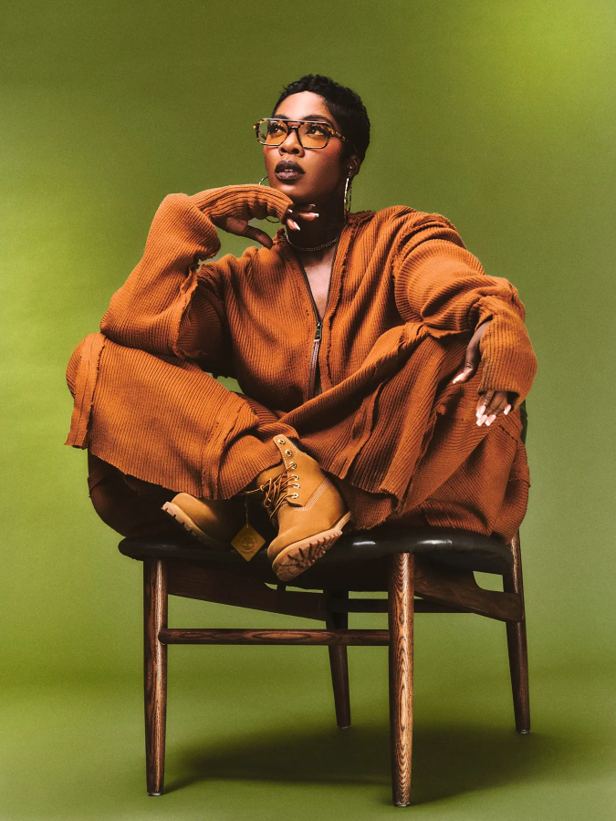 Tiwa Savage wears 6-inch boots in wheat by TIMBERLAND, jumpsuit by LEO PROTHMANN, sunglasses by HOT FUTURES and necklace by H&M