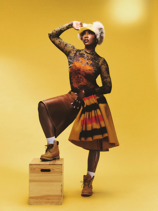 Tiwa Savage wears top by JEAN PAUL GAULTIER, hat by PARALLEL X STUDIO, earrings by ACCESSORIZE, rings by NEXT and shorter necklaces by H&M